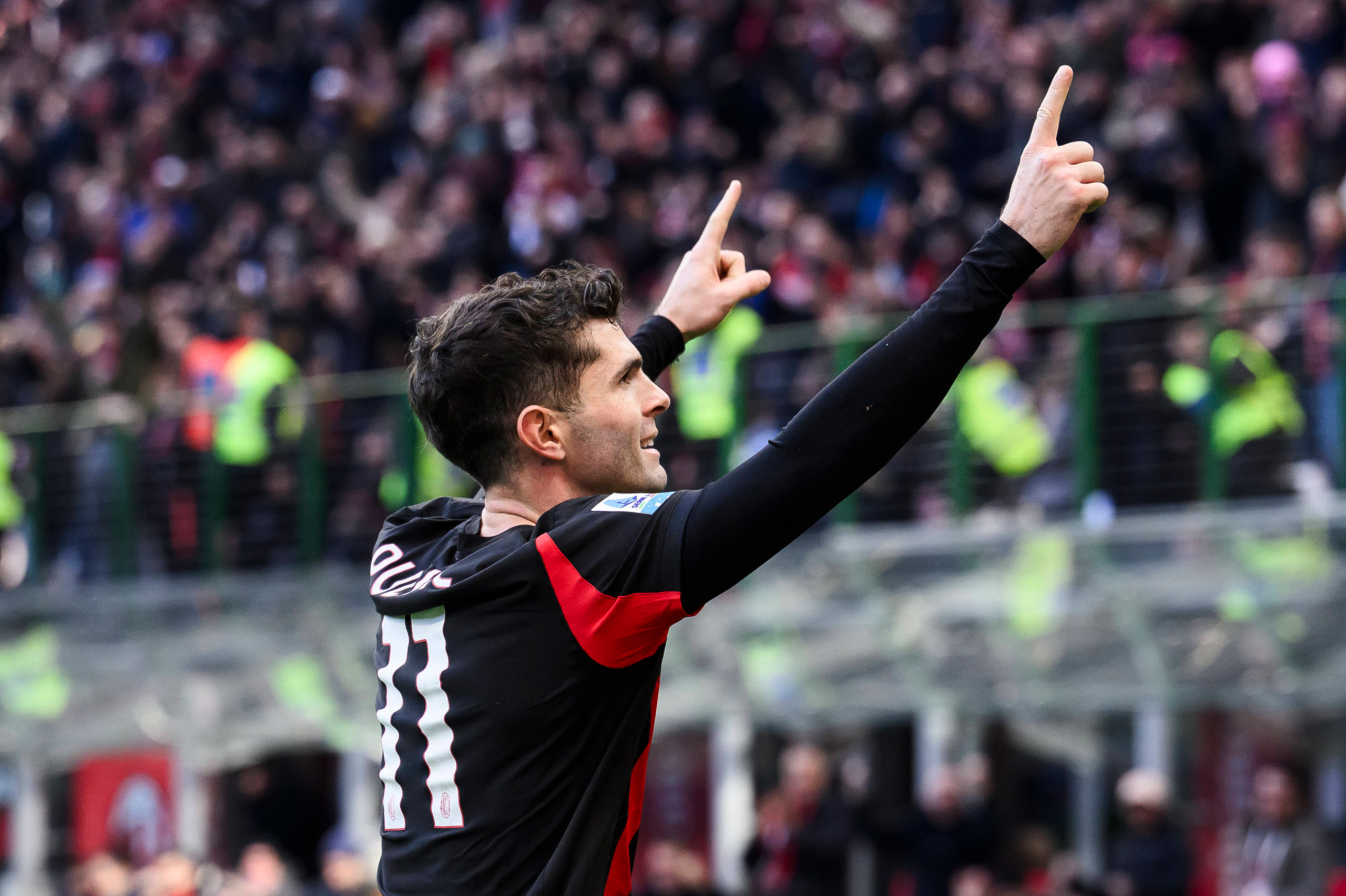 Christian Pulisic pointing with both hands raised while celebrating a goal for AC Milan.