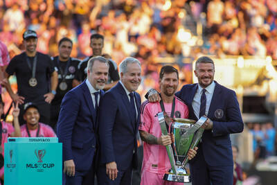 Lionel Messi and David Beckham holding the 2025 MLS Cup on a stage surrounded by Inter Miami players and personnel.